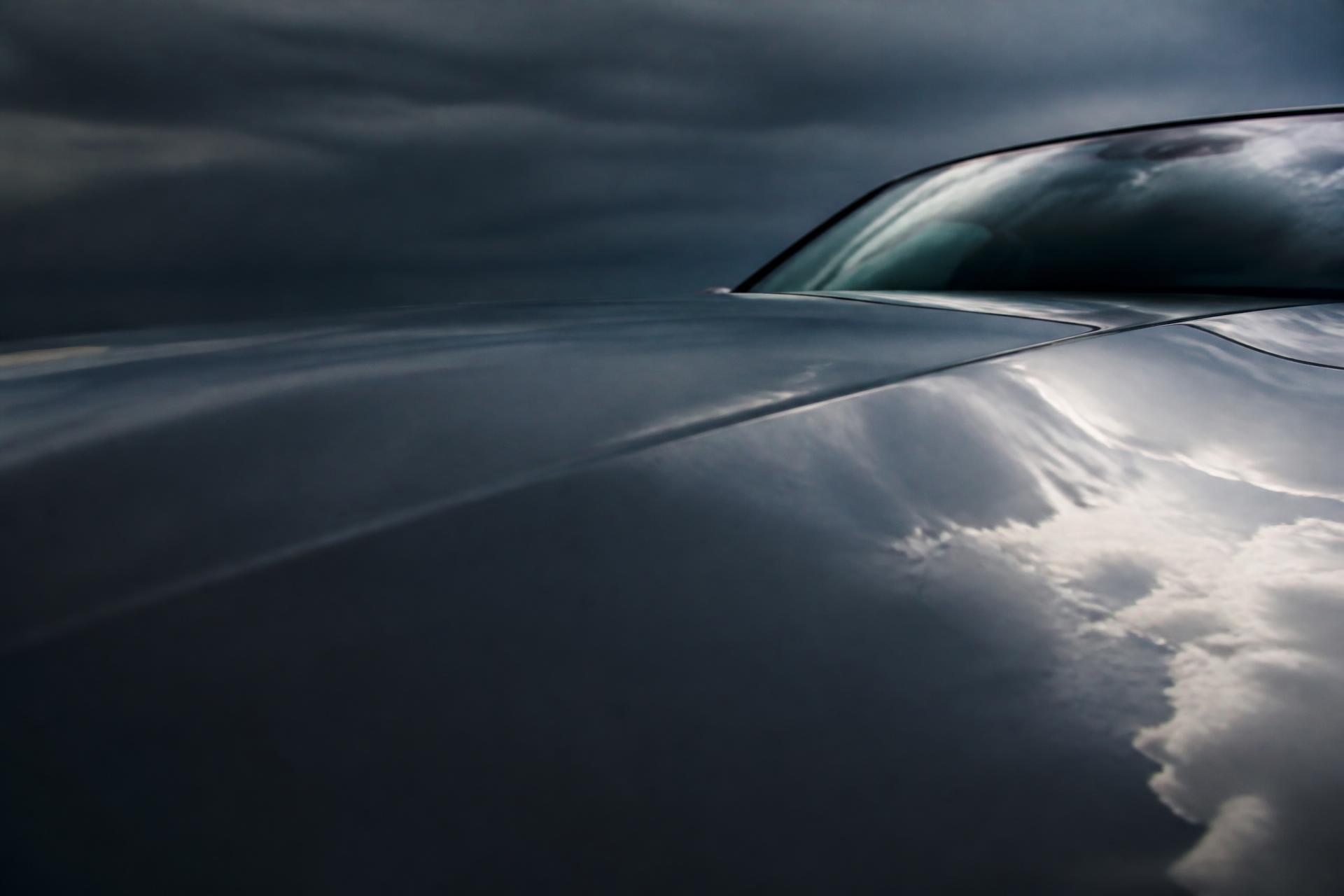 Clouds reflected across the dark paint of a clean car hood